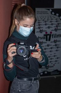volonterka u majici festivala. drži fotoaparat okrenut ka aparatu koji je slika