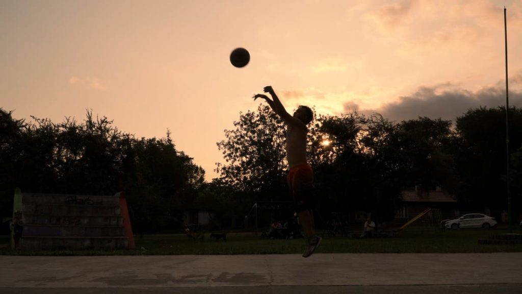 Zalazak sunca. U pomračini je muškarac na košarkaškom terenu koji baca loptu.