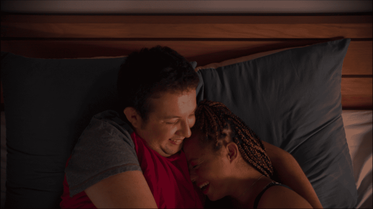 Mlađi muškarac i žena u krevetu zagrljeni. Smeju se.