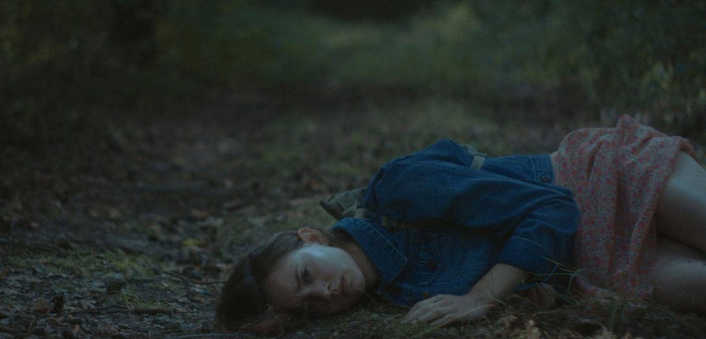 Mlada devojka leži na travi. Tužna je.