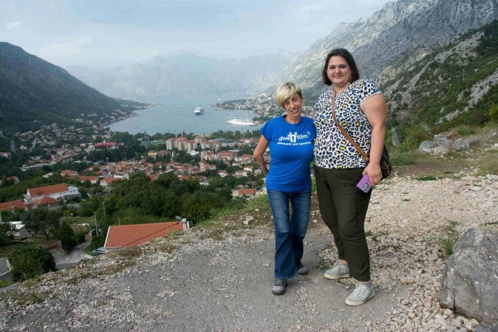 Marijana Ramić i Milesa Milinković poziraju na vidikovcu. Iza njih se vidi kotorski zaliv (kuće i more, okružene planinama).