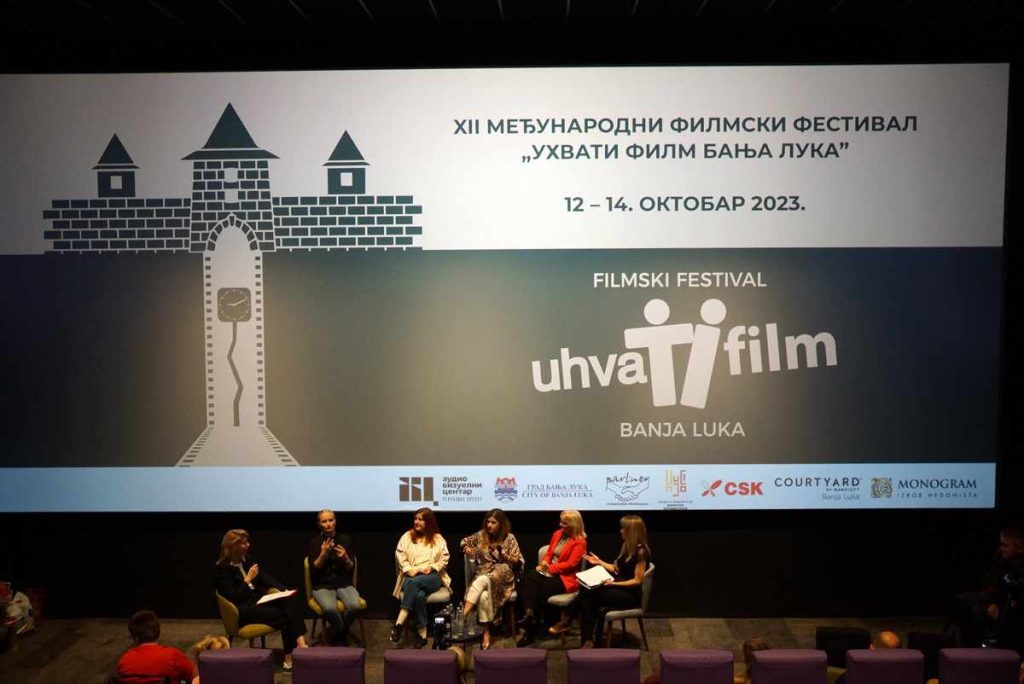 Ispred bioskopskog platna na kom je vizual Festivala, 6 žena sedi u polukrugu